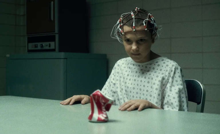 Le personnage Eleven dans la série Stranger Things plie une canette de soda posée sur une table à manger grâce au pouvoir de télékinésie.
