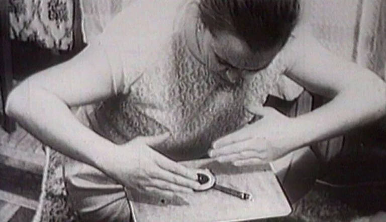 Photo de Nina Kulagina faisant une démonstration de télékinésie en déplaçant l'aiguille d'une boussole Adrianov posée sur une table.