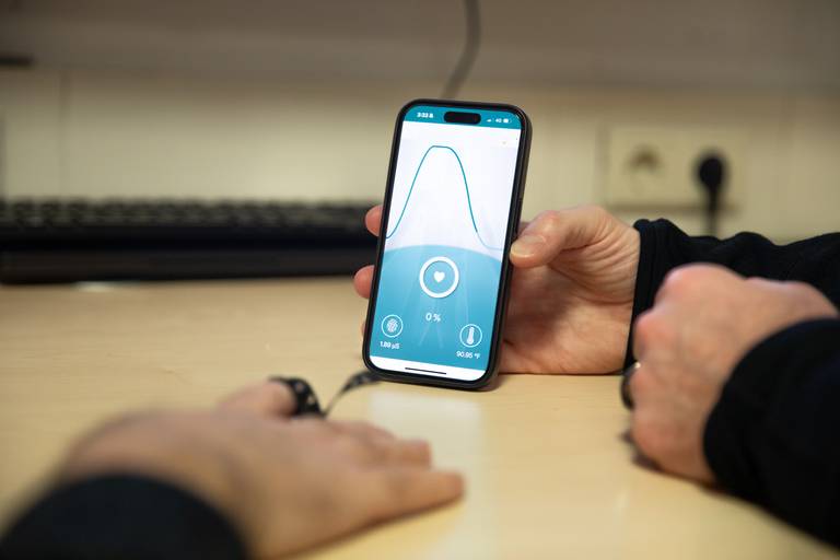 Capteur de conductance cutanée fixé au bout d'un doigt, relié à une application de biofeedback qui affiche la courbe en temps réel.