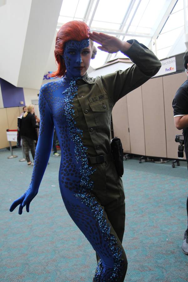 Cosplayeuse incarnant Mystique de X-Men en pleine métamorphose, moitié en combinaison bleue écaillée, moitié en uniforme militaire.