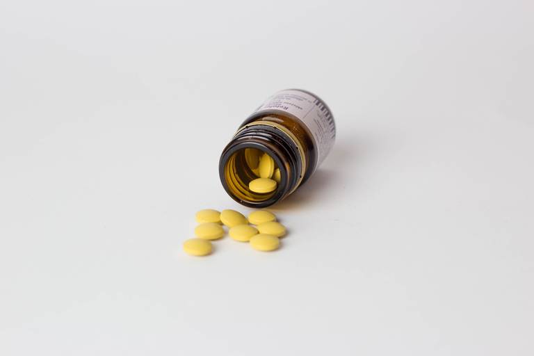 Flacon en verre ambré renversé laissant échapper des comprimés jaunes sur une surface claire, illustration de l'effet placebo.