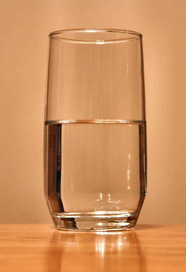 Verre d'eau posé sur une table en bois clair devant un fond neutre.