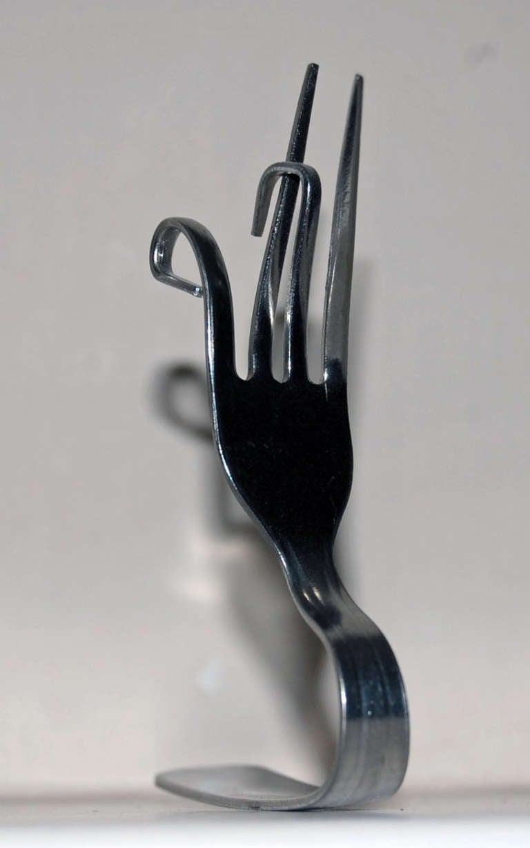 Fourchette en métal au manche plié et aux dents tordues dans tous les sens, posée sur un fond gris