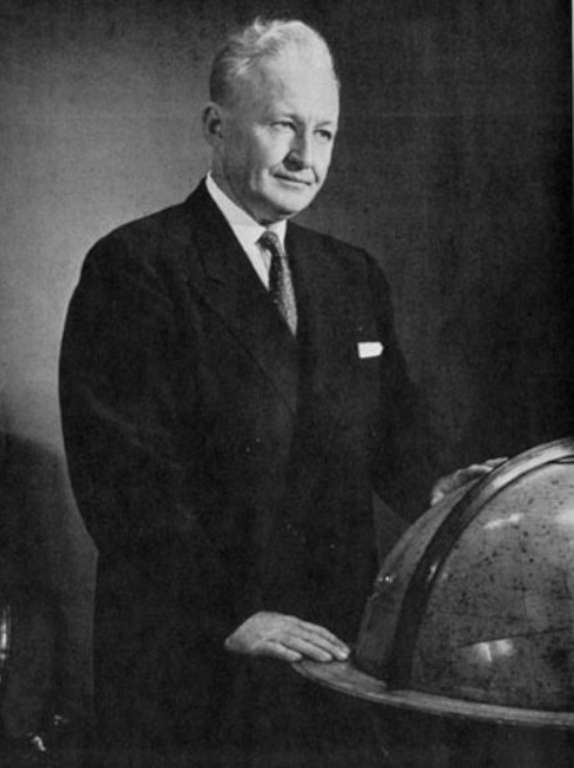 Portrait en noir et blanc de l'écrivain Harold Sherman en costume, la main posée sur un globe